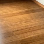 Rincón de una habitación con suelo de Piso en Bambú Macizo Caramelo, paredes blancas, rodapié, ventana y dos tomas de corriente.