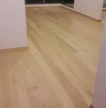 Habitación vacía con suelo de Piso de Madera Guaimaro, paredes blancas y grandes ventanales con una barandilla metálica visible en el exterior.