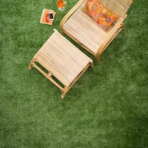 Dos sillones Pasto Sintético Deluxe con cojines sobre una superficie de pasto verde, acompañados de una mesita con un libro y un vaso de jugo de naranja.