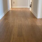 Un contenedor de acabado de suelo se sienta en un Piso en Bambú Macizo Caramelo en un pasillo con paredes y zócalos blancos.