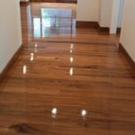 Pasillo luminoso con suelos de Piso de Madera Granadillo Miel, paredes blancas, luces empotradas en el techo y grandes ventanas en el extremo dejando entrar la luz natural.