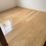 Habitación con suelo Piso de Madera Guaimaro, con zonas de brillo pulido que contrastan con otras mates. El espacio también muestra paredes blancas y un marco de puerta de madera.