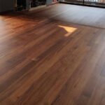 Amplia habitación con grandes ventanales, la luz del sol que entra, y Piso de Madera Zapan suelo; parcialmente cubierto puertas de cristal se abren a un balcón.