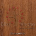 Superficie de madera con las palabras "bliss ébano pisos & maderas" y "Piso de PVC Granadillo" rodeando un diseño con incrustaciones de un árbol estilizado con puntos rojos formando una corona.