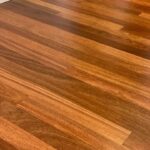 Detalle del suelo Piso de Madera Granadillo Miel en un interior residencial, con rodapiés blancos y una puerta parcialmente abierta al fondo.