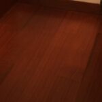 Un armario de madera con puertas ventiladas está apoyado contra una pared en una habitación con suelo de Piso de Madera Incienso y un gran ventanal a la izquierda.