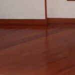 Vista interior de una habitación vacía con suelos de Piso de Madera Incienso, una escalera con peldaños de madera y barandilla metálica, y una puerta abierta que conduce a la cocina.