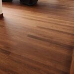 Habitación con suelo de Piso de Madera Zapan, una pequeña mesa de comedor con sillas envueltas colocadas boca abajo, escaleras a la derecha y una pared de fondo con azulejos cuadrados.