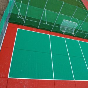 Vista aérea de una cancha de Tenis Piso de Polipropileno verde y roja con redes circundantes.