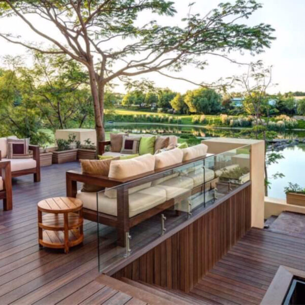 Elegante patio exterior Piso Deck WPC Cuadrado con cómodos asientos, barandilla de vidrio y vista a un tranquilo lago.