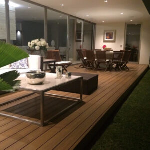 Patio exterior bien iluminado con terraza Piso Deck WPC Cuadrado, muebles y puertas corredizas de vidrio.