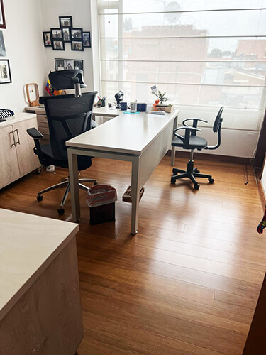 Una configuración de oficina en casa moderna con un escritorio blanco, sillas ergonómicas y una pared tipo galería.