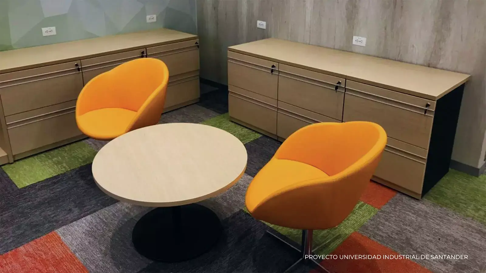 Espacio de oficina moderno con dos sillas naranjas, una mesa redonda y armarios de almacenamiento de madera, con una alfombra multicolor. superposición de texto: proyecto universidad industrial santander.