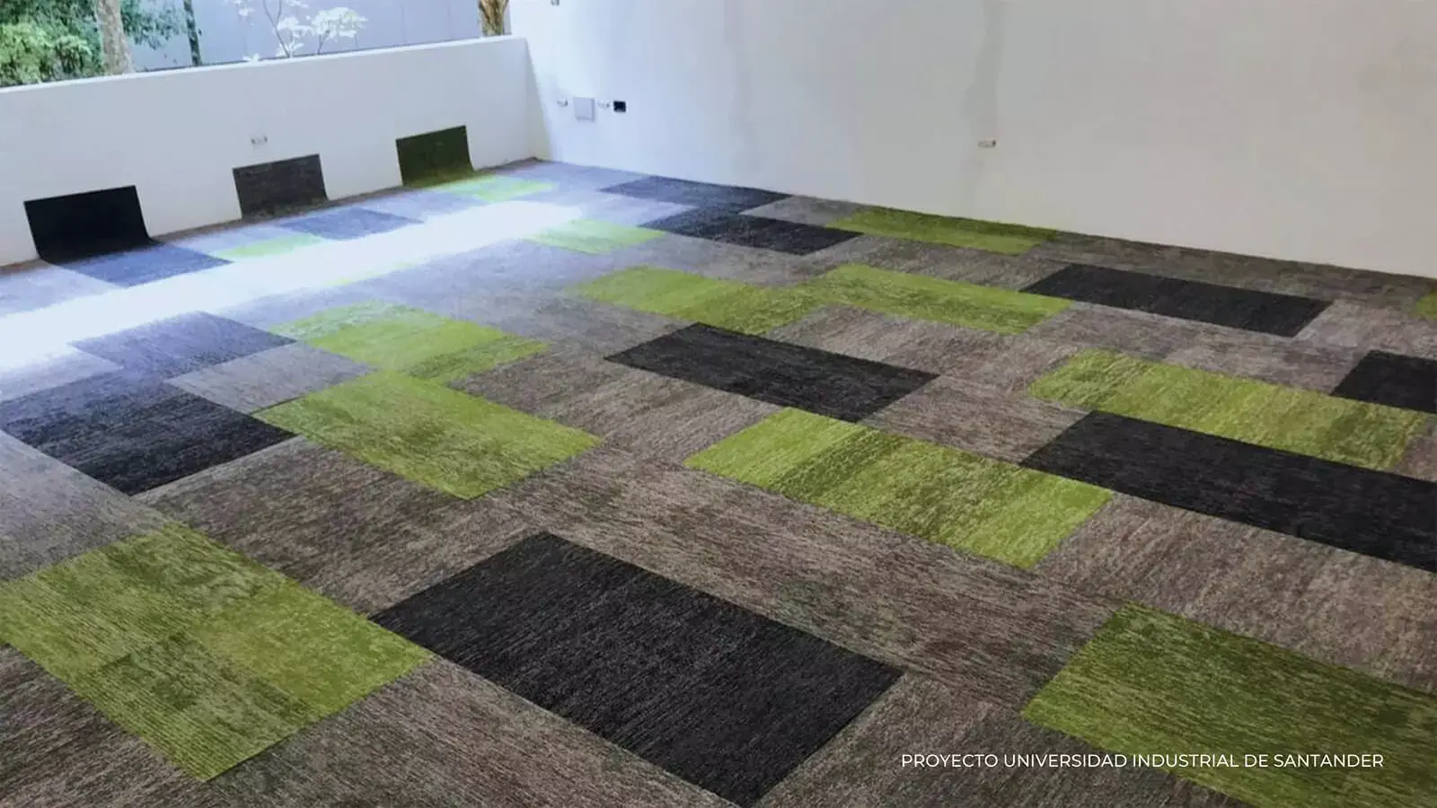 Espacio de oficina moderno que presenta una alfombra geométrica en tonos de verde, gris y negro, con un banco blanco minimalista contra la pared.