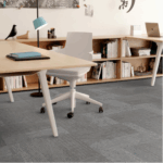 Espacio de trabajo de oficina moderno con Alfombra Arrange, escritorios de madera clara, una silla giratoria blanca, estanterías, una lámpara y elementos decorativos como arte mural de pájaros y dinosaurios.