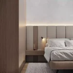 Dormitorio minimalista con cabecero beige, mesa auxiliar de madera, lámpara de lectura moderna, cama cuidadosamente hecha con ropa de cama blanca, un pequeño difusor sobre la mesa y lámina PVC para paredes en el suelo.