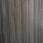 Primer plano de una superficie texturizada de Lámina PVC para paredes de color gris oscuro con patrones de vetas verticales.