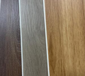 Cuatro muestras verticales de laminado de madera en distintos tonos -marrón oscuro, gris, marrón claro y miel- mostradas una al lado de la otra con separadores blancos entre ellas.