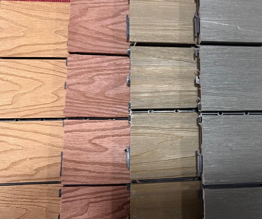 Tablas de muestra de suelos con motivos de madera en tres variaciones de color: gris oscuro, marrón claro y marrón rojizo, dispuestas en filas para su exposición.