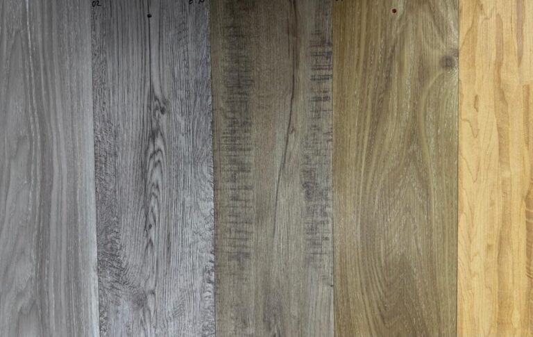 Cuatro tablones de madera de distintos tonos, desde el tostado claro al gris oscuro, están dispuestos horizontalmente, mostrando distintos patrones y colores de las vetas de la madera.