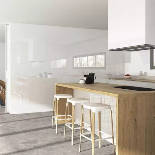Cocina moderna con isla de madera, tres sillas altas y vitrocerámica empotrada. El espacio cuenta con una pared de grandes ventanales y una decoración minimalista en tonos neutros.